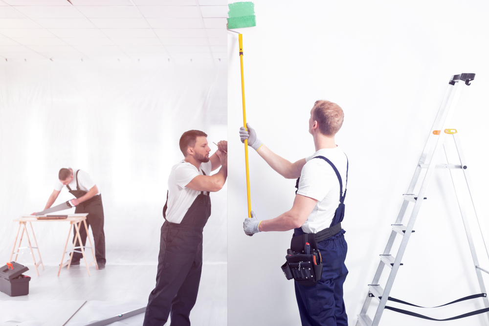 Craftsman painting white wall green while finishing interior