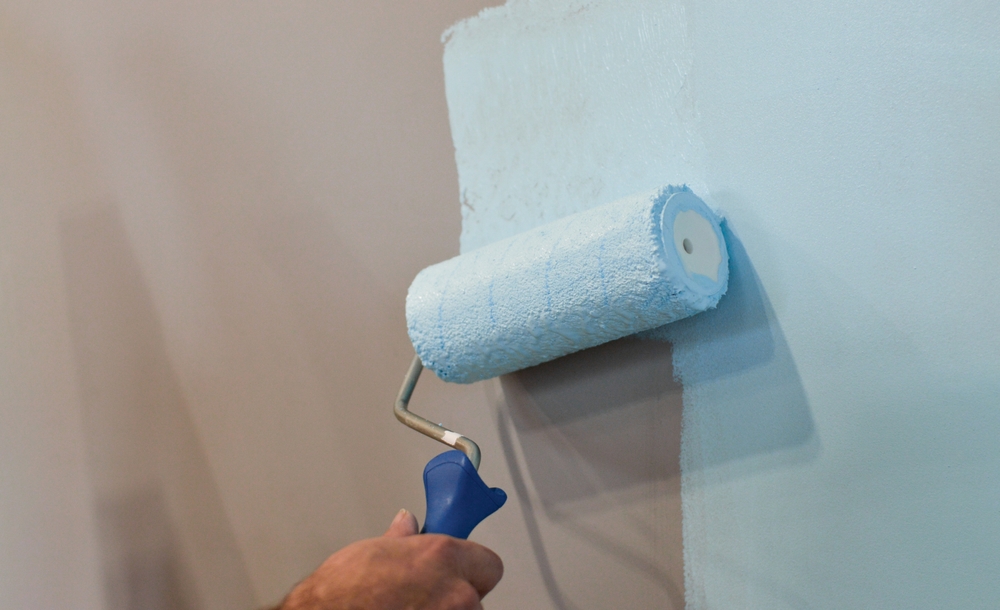 During the apartment remodeling process, a worker uses a paint roller to cover the wall surface with white color, transforming the living space with new paint.